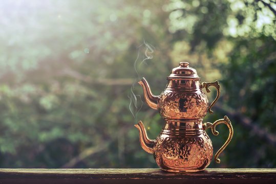 Clear tulip-shaped Turkish tea glasses filled with amber tea alongside traditional çaydanlık double teapot system on ornate metal tray, showcasing Turkish tea ceremony practices