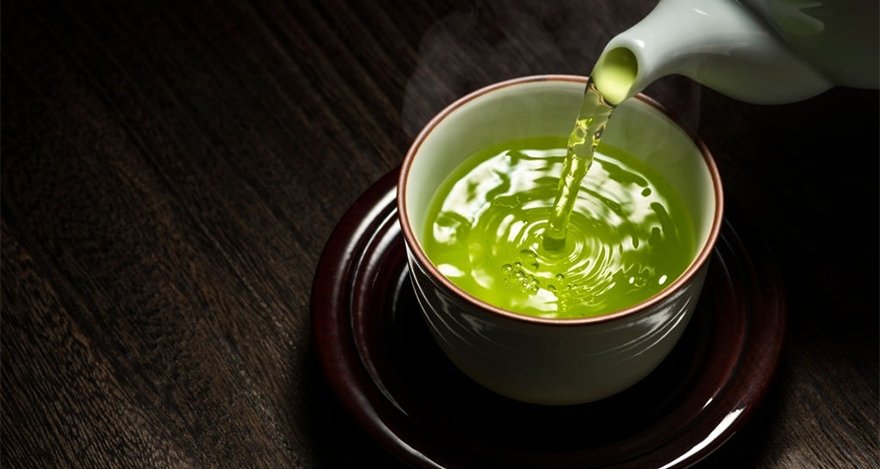 japanese tea cup with green tea pouring out from a white teapot.